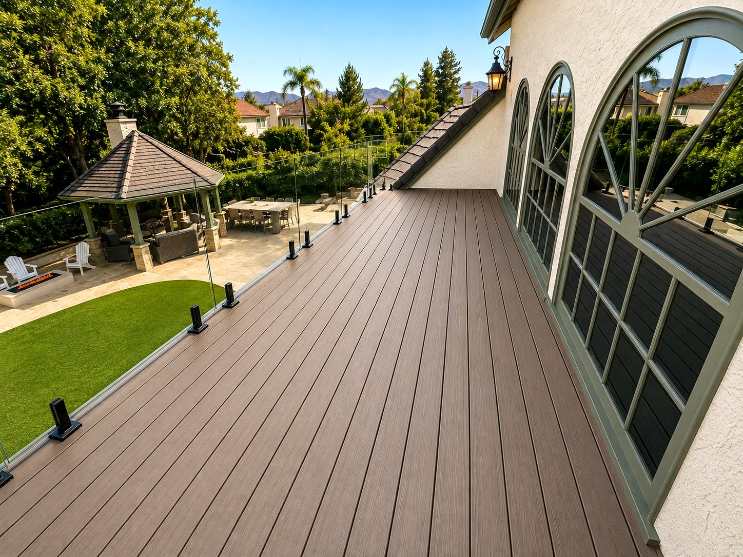 Rooftop composite deck with glass railing overlooking a backyard patio and gazebo — Los Angeles